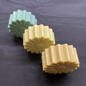 3 savons en forme de marguerite posés sur la tranche, sur une nappe noire.