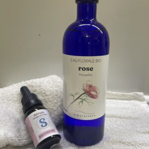 Bouteille bleu contenant de l'eau de rose et flacon de sérum posé à côté